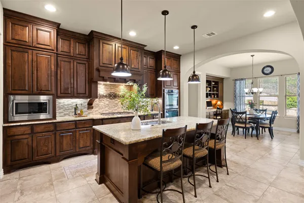 a kitchen with stainless steel appliances granite countertop a stove a refrigerator a sink a dining table and chairs with wooden floor