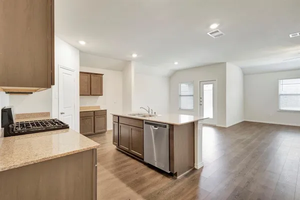 a kitchen with stainless steel appliances granite countertop a stove top oven a sink dishwasher a refrigerator and a dining table with wooden floor