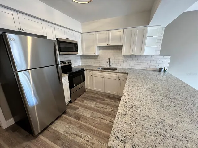 a kitchen with granite countertop a refrigerator a sink a stove a microwave and cabinets