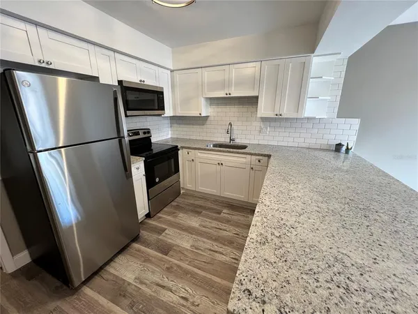 a kitchen with granite countertop a refrigerator a sink a stove a microwave and cabinets