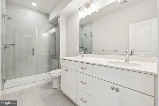 a spacious bathroom with double sink a toilet a shower and a mirror