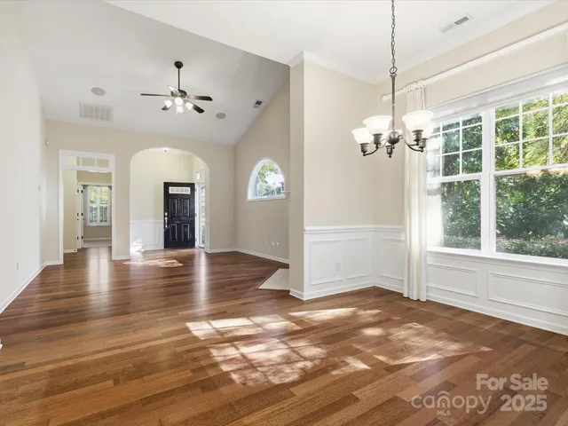 an empty room with wooden floor chandelier and windows