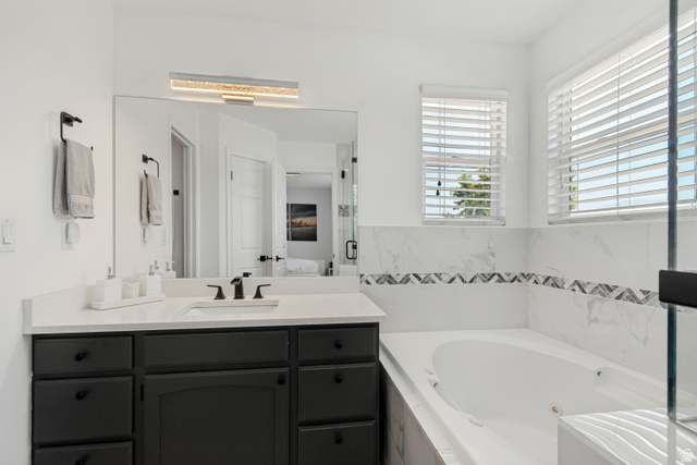 4752 South 4075th Street West Roy, UT 84067 - Photo 11 of 28 Spacious bathroom featuring a built-in soaking tub, a vanity with a white countertop and dark cabinetry, and a large wall-mounted mirror with an integrated light fixture