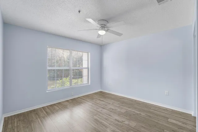 an empty room with wooden floor ceiling fan and windows