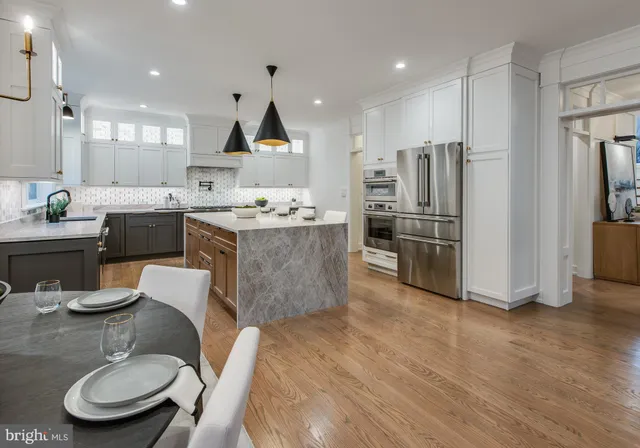 a kitchen with stainless steel appliances kitchen island granite countertop a refrigerator a stove a sink a dining table and chairs with wooden floor