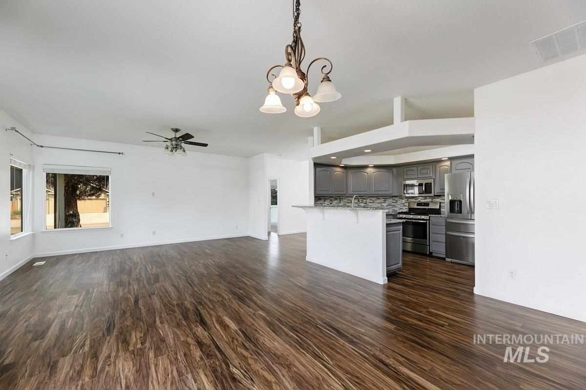 2575 S Bayou Meridian, ID 83642 - Photo 14 of 30 Open-concept living space with wood-finish flooring, a contemporary ceiling fan, and a kitchen featuring stainless steel appliances, gray cabinetry, and a tile backsplash