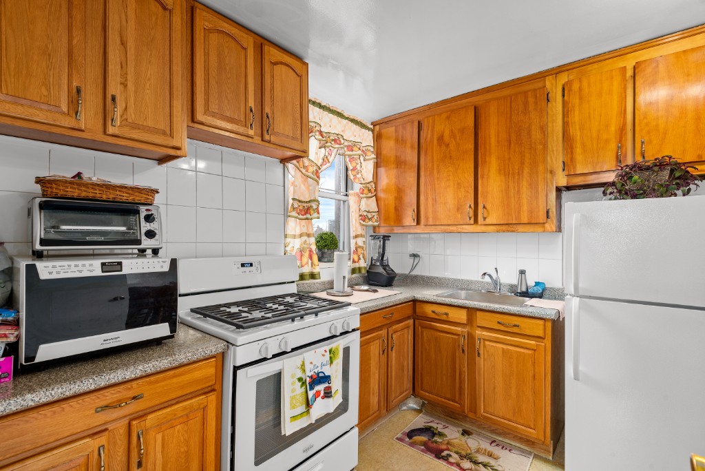 60-11 Broadway, Unit 3C Queens, NY 11377 - Photo 10 of 18 a kitchen with stainless steel appliances a stove a sink and a refrigerator with wooden cabinets