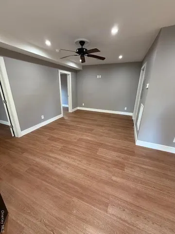 a view of an empty room with wooden floor and a ceiling fan