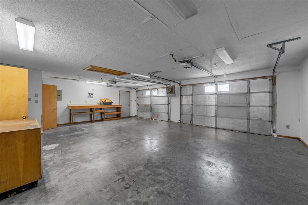 3301 Loma Vista Drive Waco, TX 76708 - Photo 22 of 29 Spacious garage featuring two garage doors, concrete flooring, overhead lighting, an exposed workbench, and a wood-finish cabinet