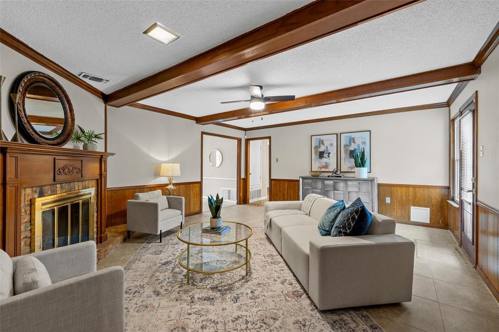 3301 Loma Vista Drive Waco, TX 76708 - Photo 6 of 29 Spacious living area featuring a wood-panel accent wall, exposed ceiling beams, and a fireplace with a brick surround