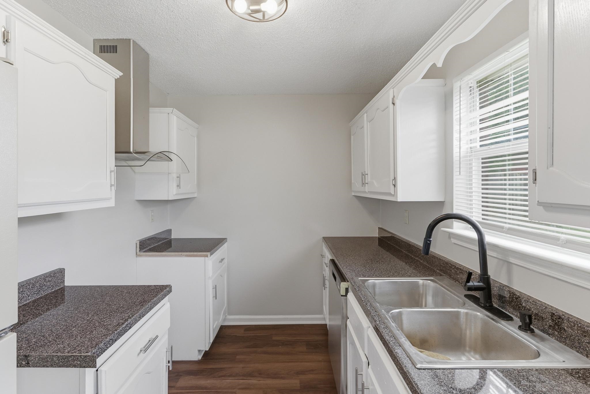 4101 Long Creek Road Memphis, TN 38125 - Photo 4 of 36 Galley kitchen featuring white cabinetry, dark speckled countertops, stainless steel dual basin sink with a matte black faucet, and wood-finish flooring