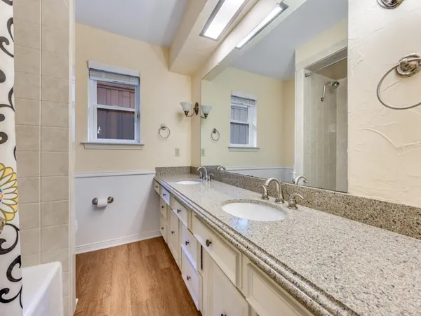 a bathroom with a granite countertop double vanity sink a mirror and a shower