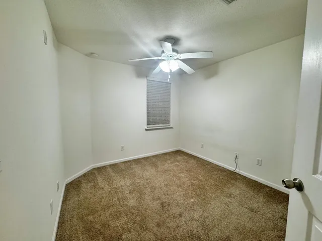 an empty room with a chandelier fan and windows