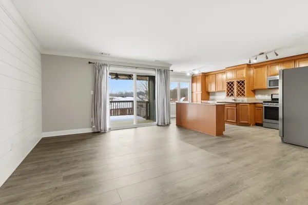 an empty room with wooden floor and kitchen view