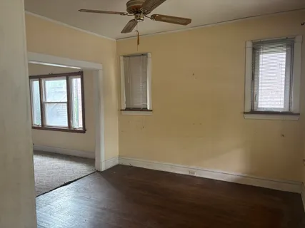 an empty room with wooden floor chandelier fan and windows