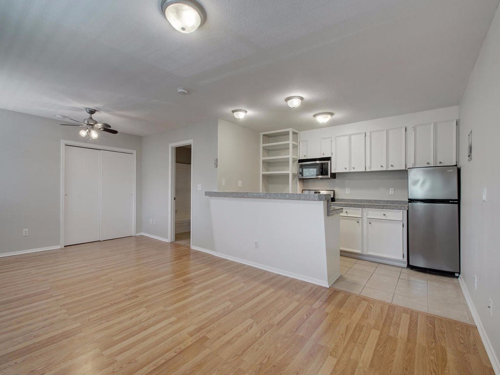 a kitchen with granite countertop a refrigerator oven a sink dishwasher and white cabinets with wooden floor