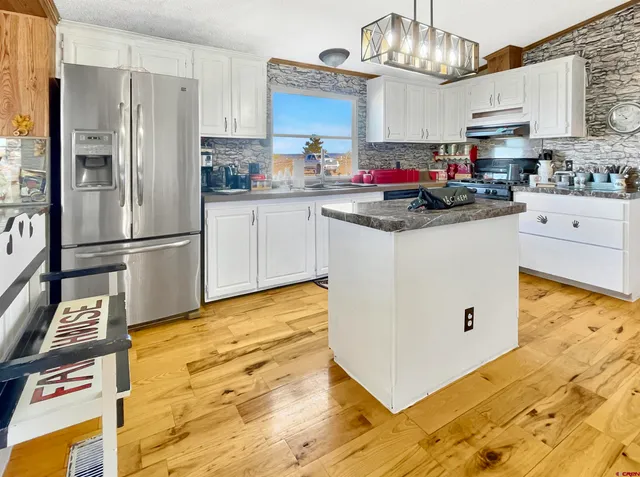 a kitchen with stainless steel appliances granite countertop a refrigerator a stove a sink dishwasher and white cabinets with wooden floor