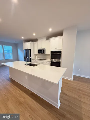 a large kitchen with kitchen island a stove a sink a refrigerator and white cabinets with wooden floor