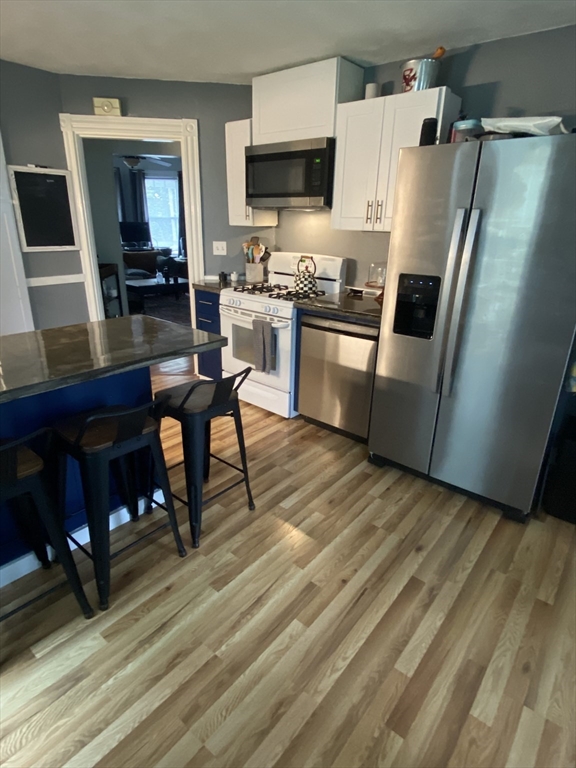 54 Olney Street Watertown, MA 02472 - Photo 4 of 28 a kitchen with stainless steel appliances a stove a refrigerator a sink a dining table and chairs with wooden floor