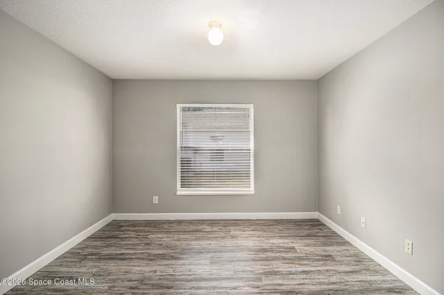 a view of an empty room with window and wooden floor