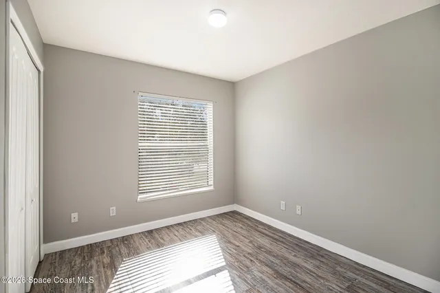 a view of an empty room with wooden floor and a window