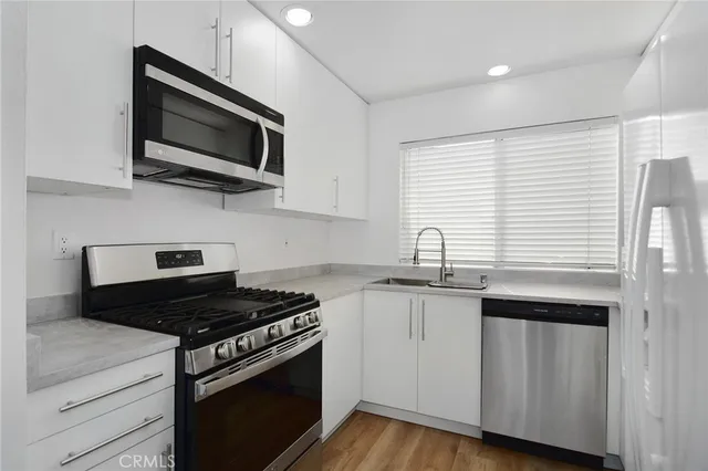 a kitchen with stainless steel appliances a sink a stove a microwave and wooden floors