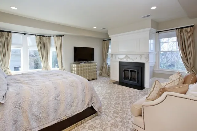 a spacious bedroom with a bed a fireplace and a flat tv screen