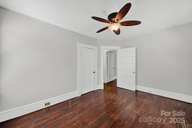 a view of an empty room with wooden floor and a ceiling fan