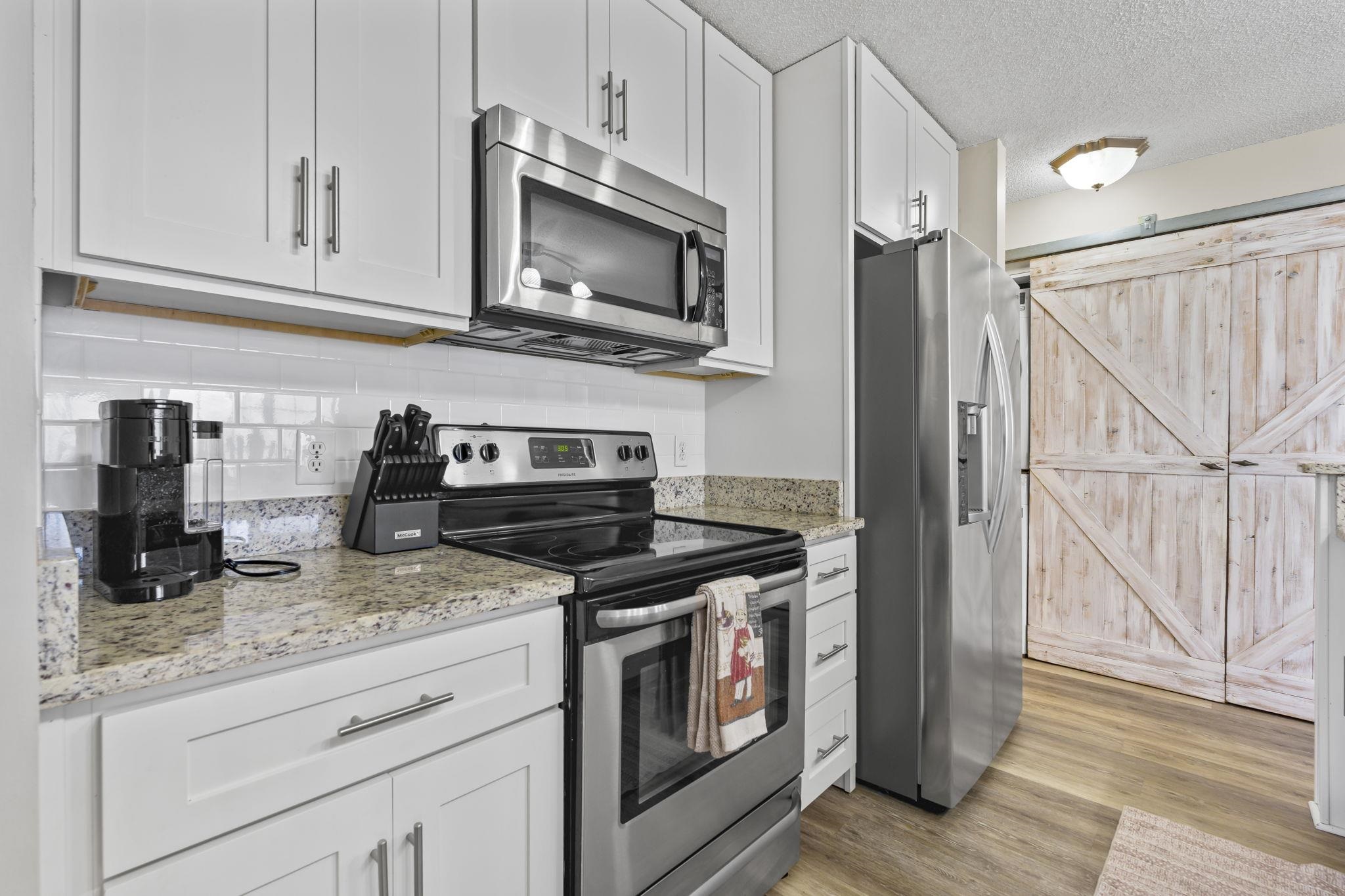 4353 Spa Drive, Unit 909 Little River, SC 29566 - Photo 11 of 39 Kitchen with stainless steel appliances, light stone countertops, white cabinetry, a textured ceiling, and light wood finished floors