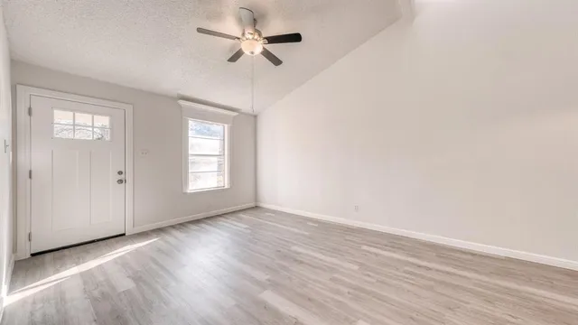 an empty room with wooden floor ceiling fan and windows
