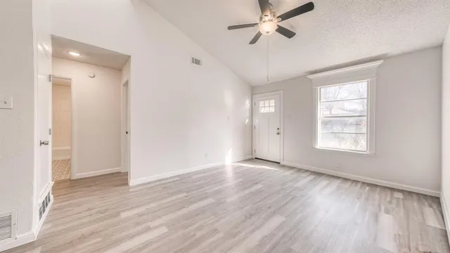 an empty room with wooden floor a ceiling fan and windows