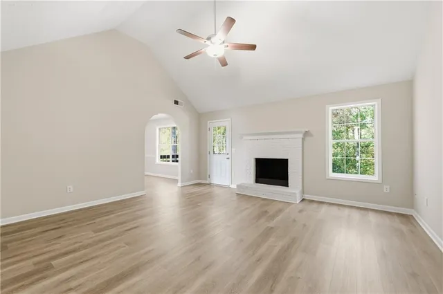 an empty room with wooden floor a ceiling fan a fireplace and windows