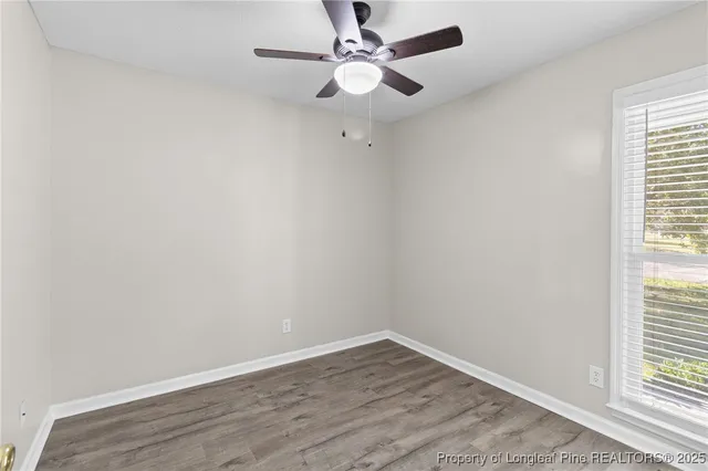 an empty room with wooden floor fan and windows