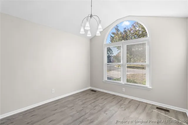 an empty room with wooden floor chandelier and windows