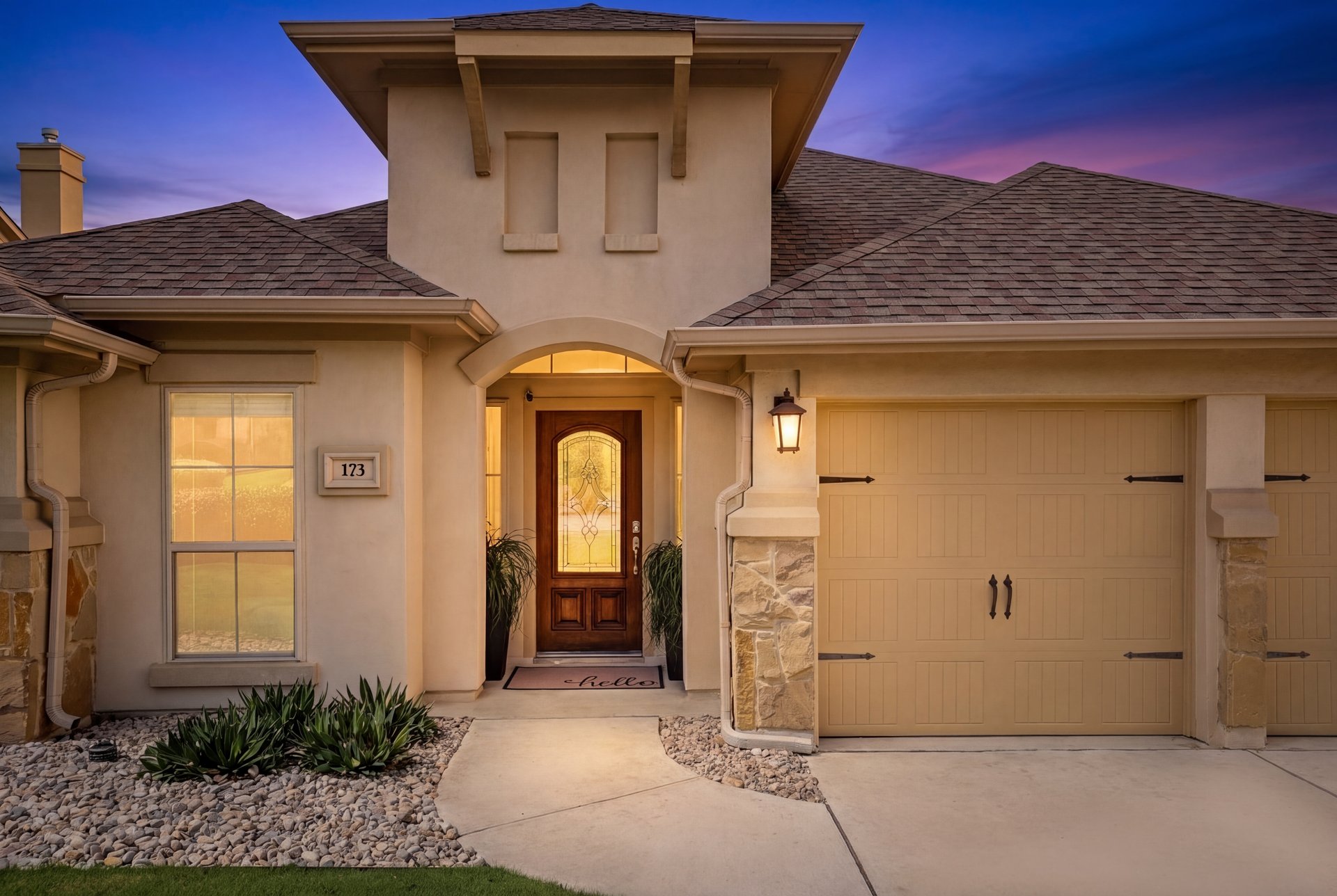 173 Santa Maria Street Georgetown, TX 78628 - Photo 3 of 39 Stucco exterior featuring a prominent arched entry, a decorative wood and glass paneled front door, an integrated two-car garage with carriage-style doors, stone accents, and a shingled roof