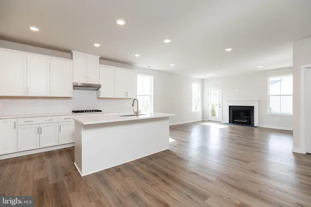 a kitchen with granite countertop a stove top oven a sink and white cabinets with wooden floor