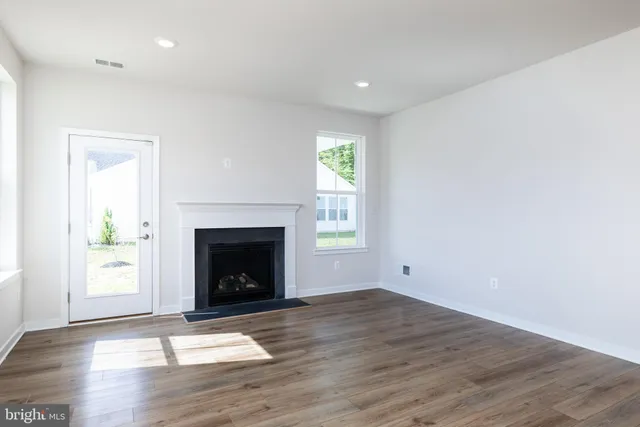 a view of an empty room with wooden floor fireplace and a window