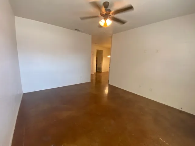 a view of an empty room with chandelier fan and wooden floor
