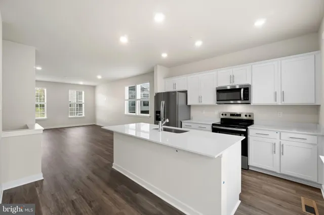 a kitchen with stainless steel appliances a stove top oven a sink dishwasher a refrigerator and white cabinets with wooden floor