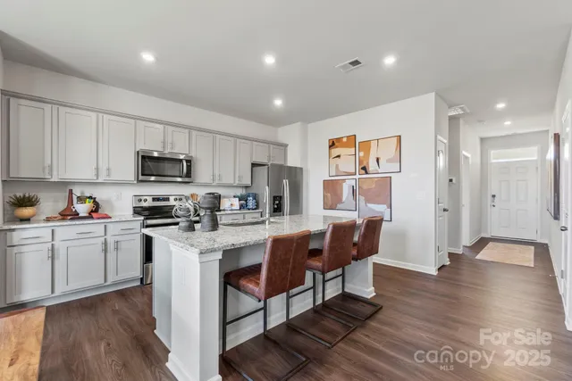 a kitchen with stainless steel appliances granite countertop a refrigerator a stove top oven a sink dishwasher and white cabinets with wooden floor