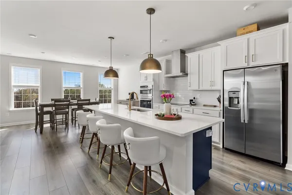 a kitchen with stainless steel appliances granite countertop a stove a sink a refrigerator a dining table and chairs with wooden floor