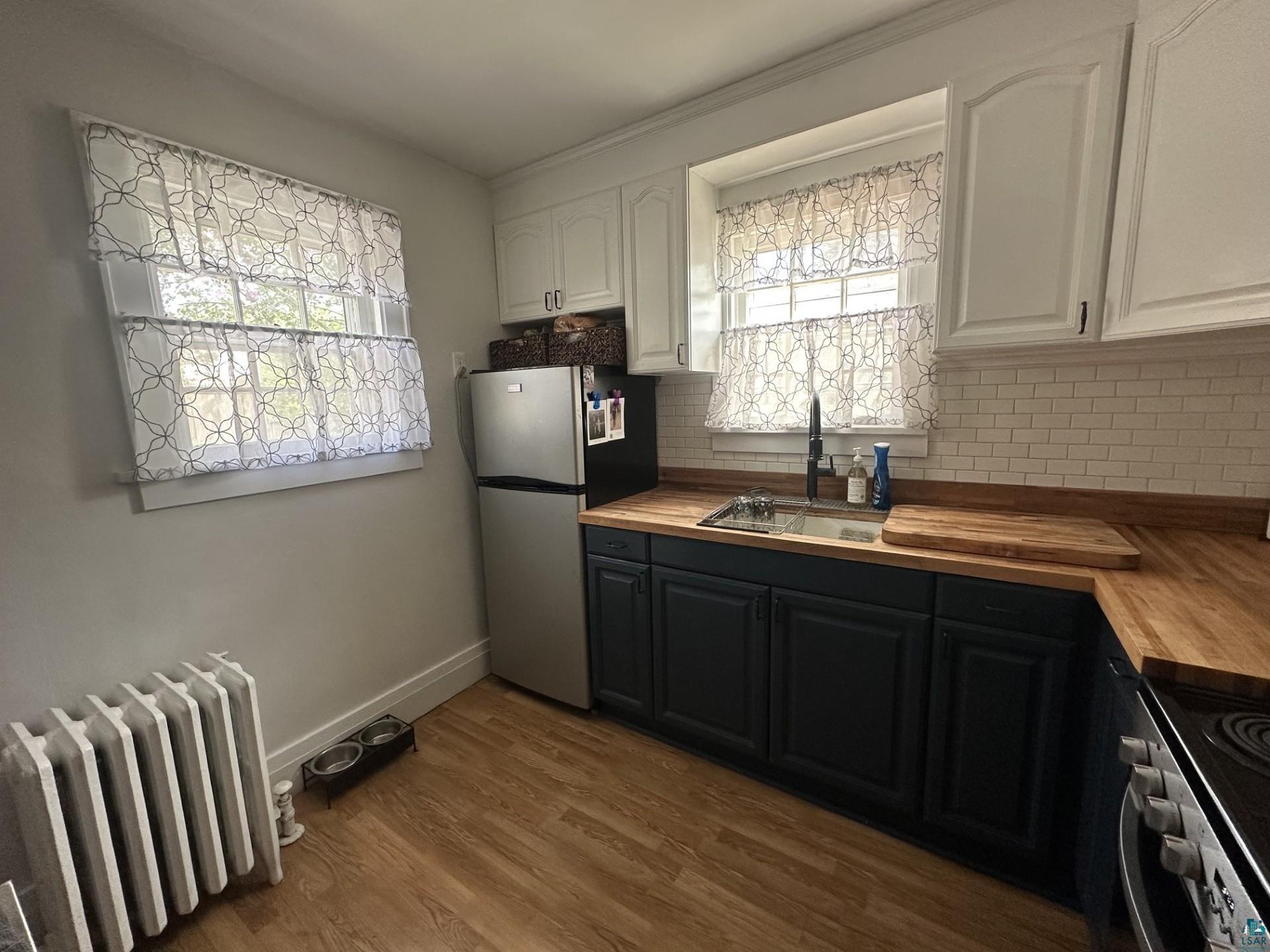 208 Chestnut Street Cloquet, MN 55720 - Photo 15 of 24 Kitchen featuring wood-finish flooring, white subway tile backsplash, butcher block countertops, stainless steel appliances, and contrasting dark lower cabinetry with white upper cabinetry
