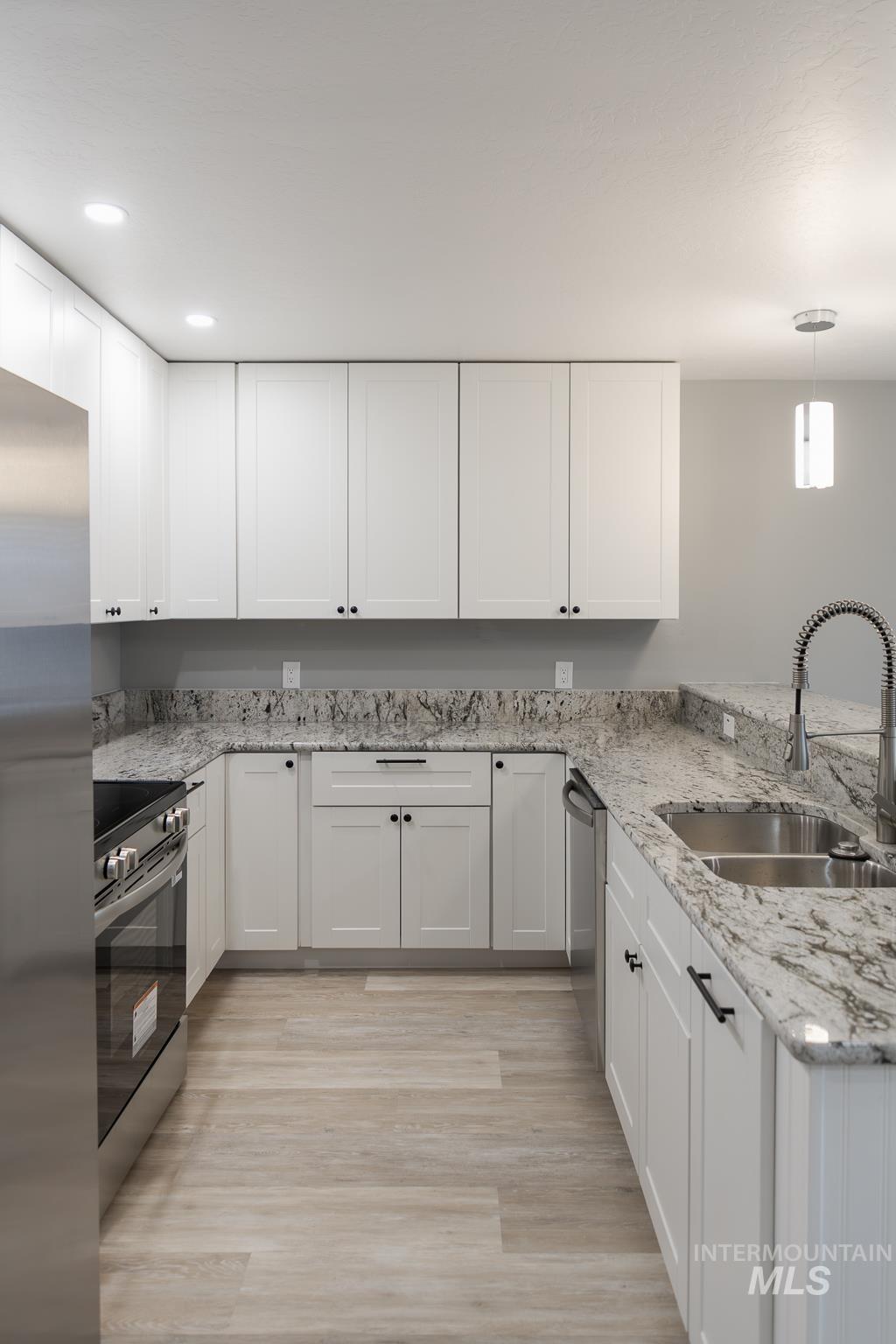 297 Southwest 6th Street, Unit 1 Ontario, OR 97914 - Photo 4 of 50 Kitchen featuring light stone counters, stainless steel appliances, light wood-type flooring, and white cabinets