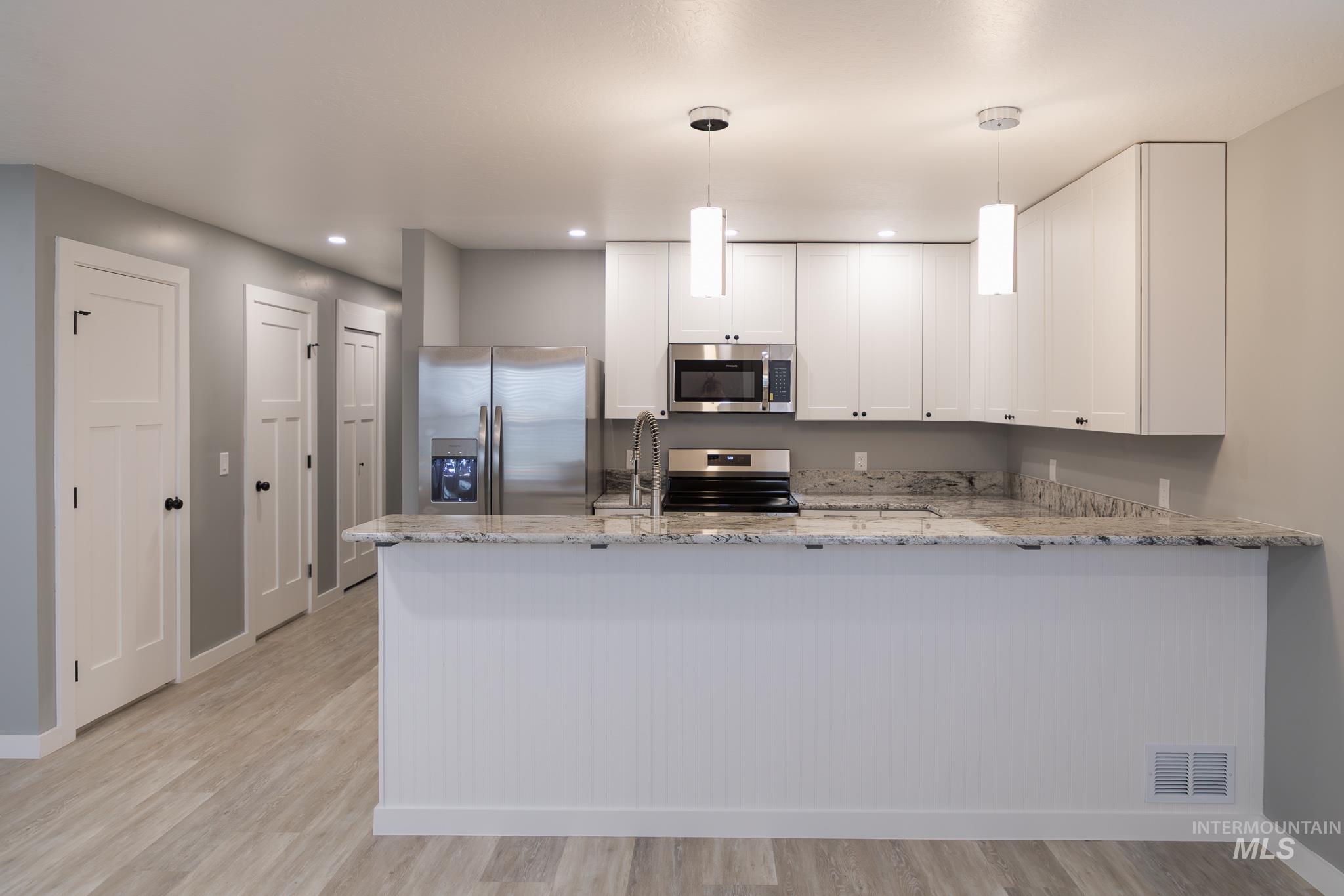 297 Southwest 6th Street, Unit 1 Ontario, OR 97914 - Photo 5 of 50 Kitchen featuring a peninsula, stainless steel appliances, white cabinets, light stone countertops, and decorative light fixtures