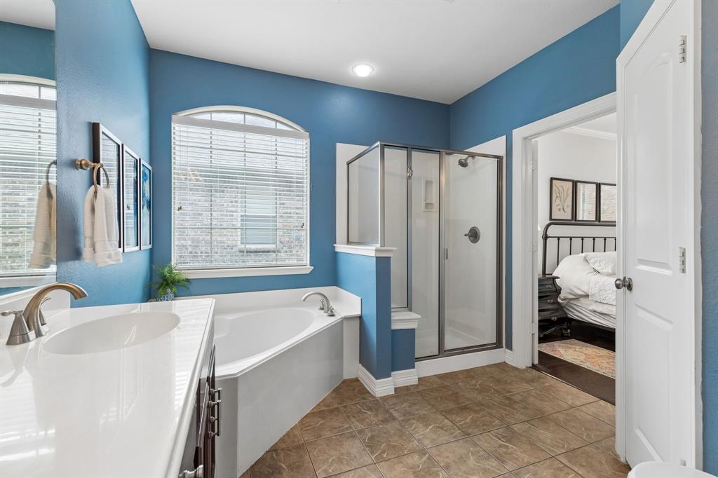 960 Remuda Road Frisco, TX 75033 - Photo 18 of 39 Bathroom featuring a corner soaking tub with an arched window, a glass-enclosed shower, and a vanity with an integrated sink and brushed nickel faucet