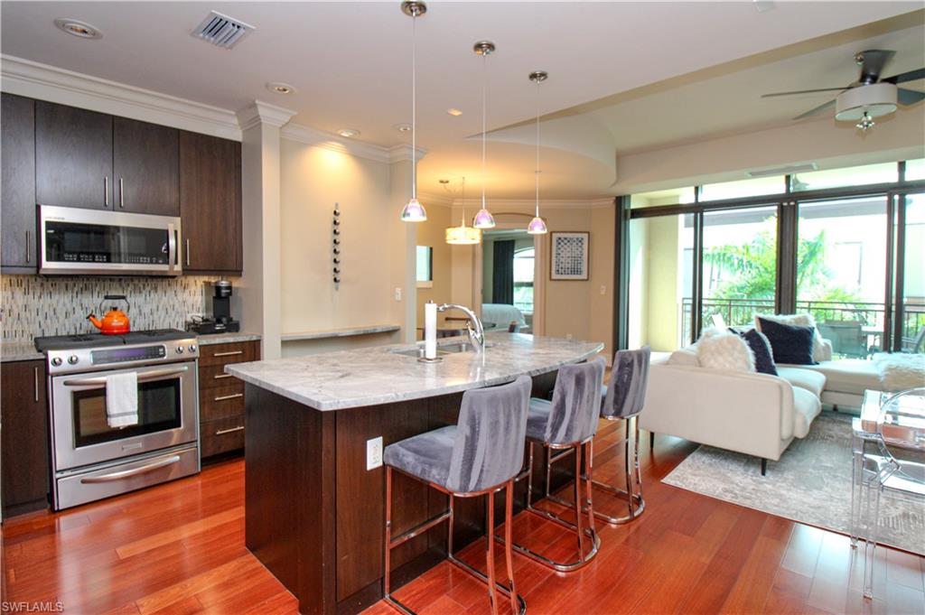 9123 Strada Place, Unit 7410 Naples, FL 34108 - Photo 25 of 50 Kitchen with light hardwood / wood-style flooring, appliances with stainless steel finishes, an island with sink, pendant lighting, and a breakfast bar