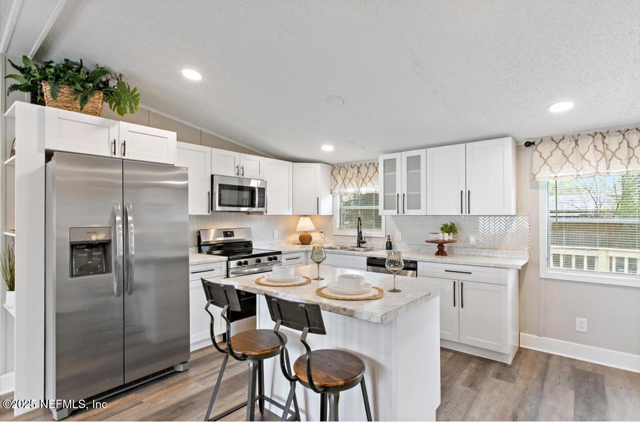 3032 Snell Street Jacksonville, FL 32218 - Photo 6 of 17 a kitchen with stainless steel appliances a refrigerator a stove a sink dishwasher and white cabinets with wooden floor