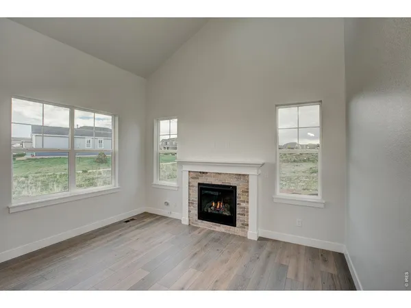 a view of an empty room with wooden floor fireplace and a window