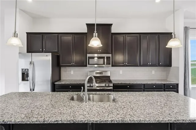 a kitchen with kitchen island granite countertop a refrigerator a stove and a sink with wooden floor