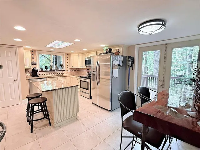 a kitchen with stainless steel appliances kitchen island granite countertop a refrigerator a stove a sink dining table and chairs with wooden floor